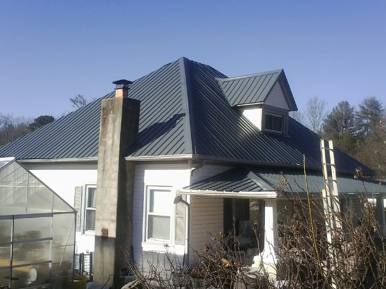 Dark blue standing seam metal roof on a white farmhouse with dormer — Slate & Tile Roof Repair by Roofing Brothers in Suwanee