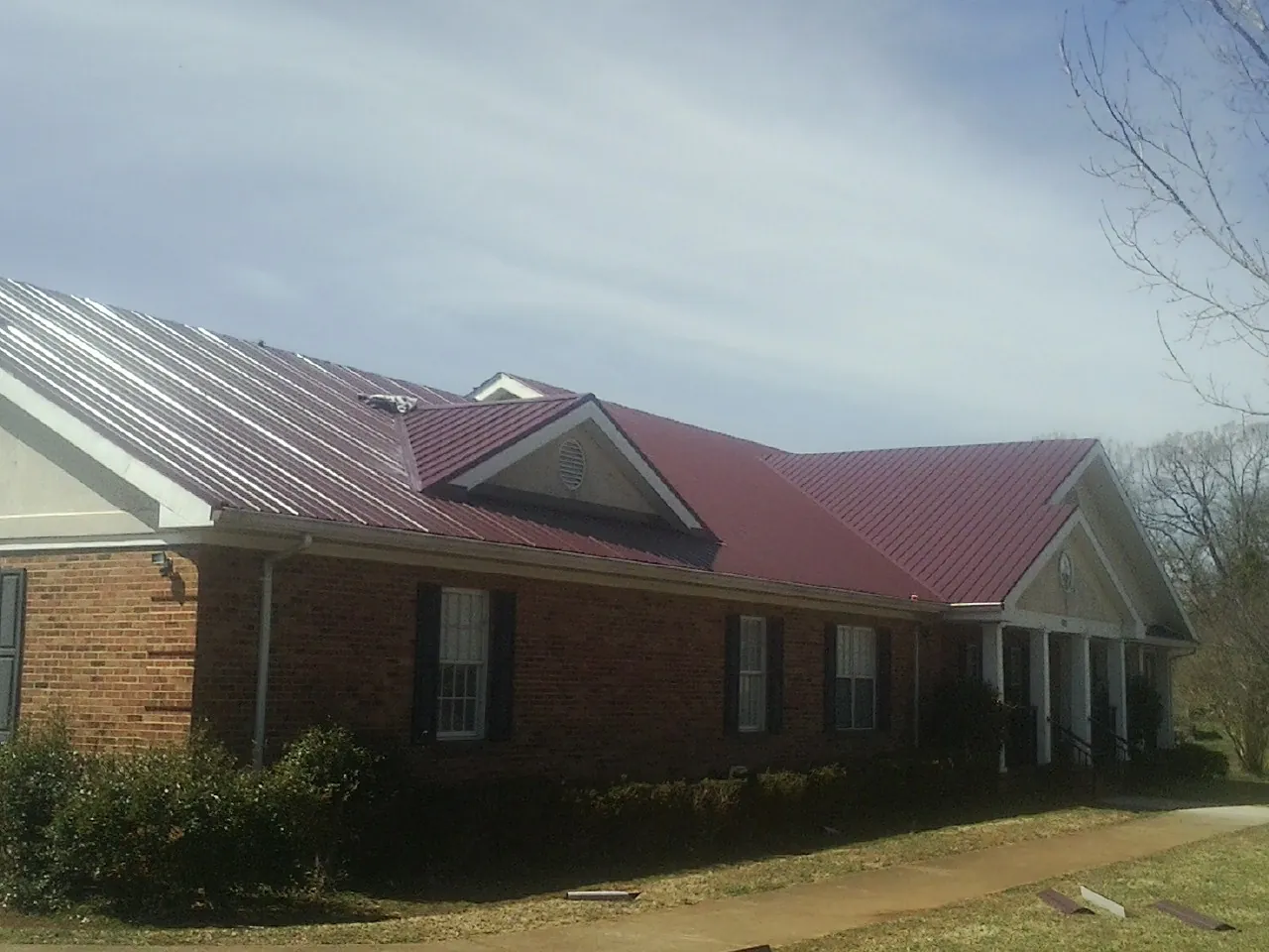 Red metal roof with gabled entries on a long brick building, from a Hail Damage Roof Repair job in Suwanee