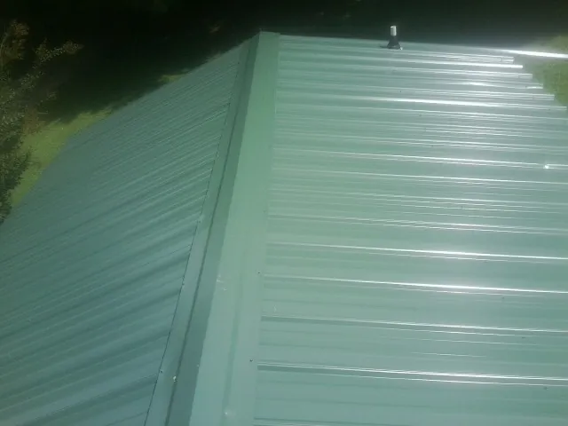 New green metal panels meeting at the ridge of a roof — Flat Roof Repair work by our crew in Suwanee